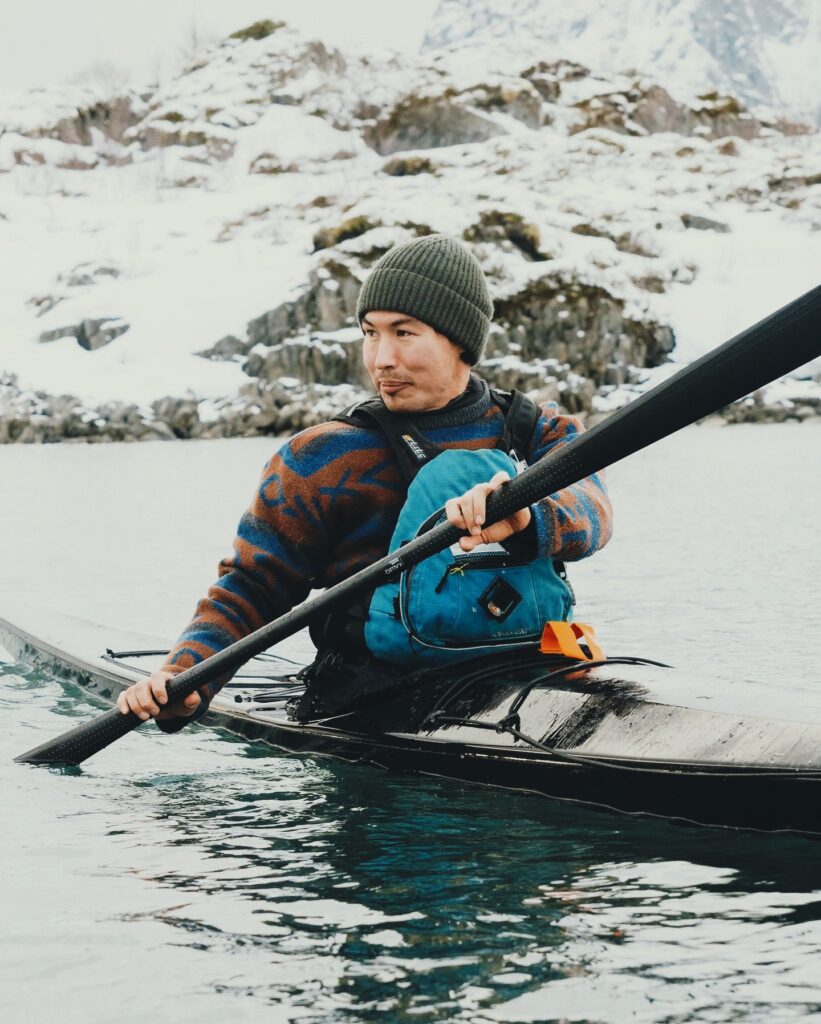 Sea kayaker using a carbon‑fiber Gearlab Greenland paddle Kalleq at sunrise, blade quietly slicing calm Arctic water.