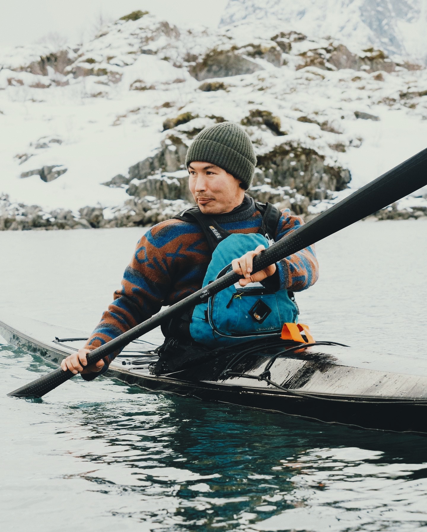 Sea kayaker using a carbon‑fiber Gearlab Greenland paddle Kalleq at sunrise, blade quietly slicing calm Arctic water.